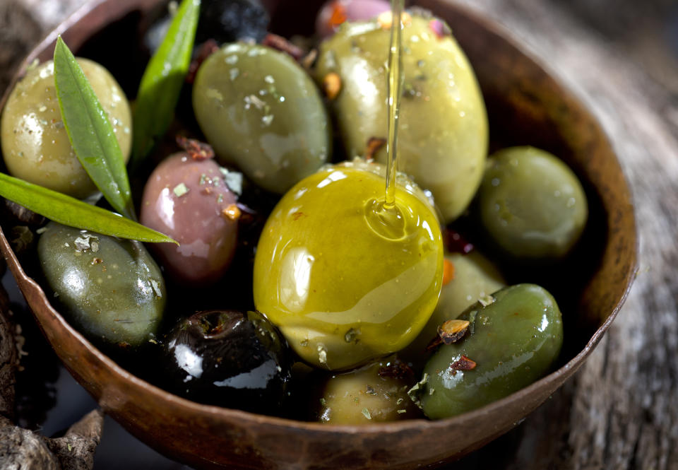 Oliven und Olivenblätter, getränkt in Olivenöl, in einem Schälchen. 