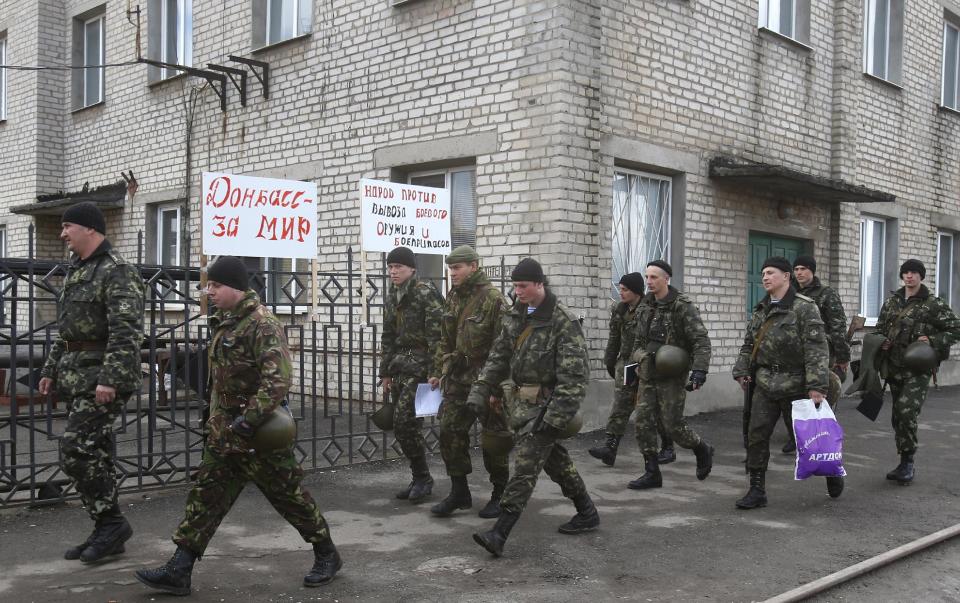 Soldiers walk near the armory Ukrainian army in the village of Poraskoveyevka, eastern Ukraine, Thursday, March 20, 2014. The disheveled men barricading the muddy lane leading into a military base in this eastern Ukraine village say they're taking a stand to defend Russian-speakers. Placards read at right "Donbass for peace" and at left "People against the export of military weapons and ammunition" (AP Photo/Sergei Grits)