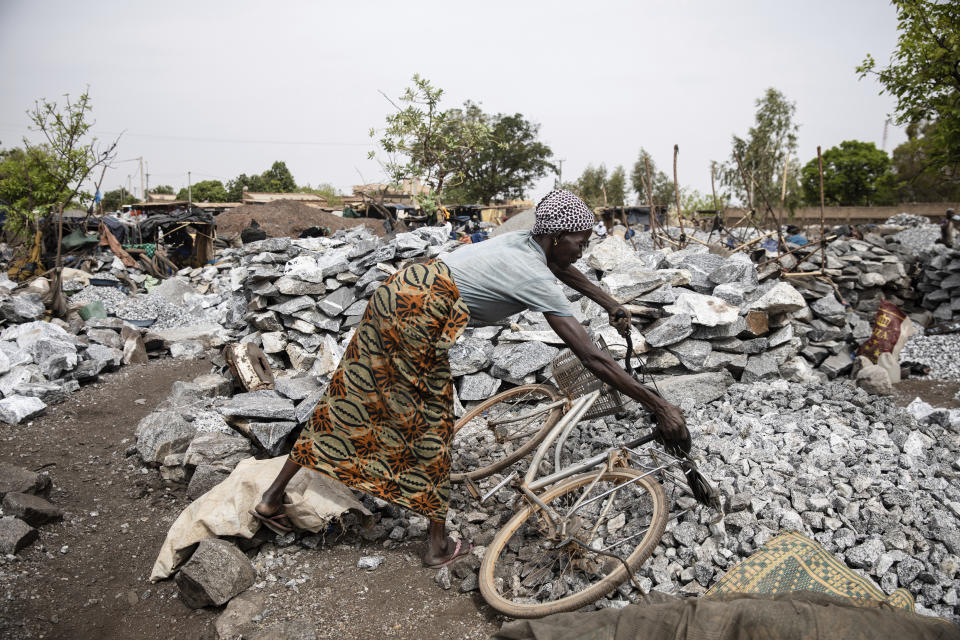 A woman working in a Pissy granite mine in Ouagadougou, Burkina Faso, Monday April 25, 2022 drops her bicycle on the ground. he influx of people displaced by the country's rapidly rising Islamic violence is causing competition among the approximately 3,000 people working at the granite mine. At least 500 displaced people started working at the mine last year making it harder for the original miners to earn a living, said Abiba Tiemtore, head of the site. (AP Photo/Sophie Garcia)