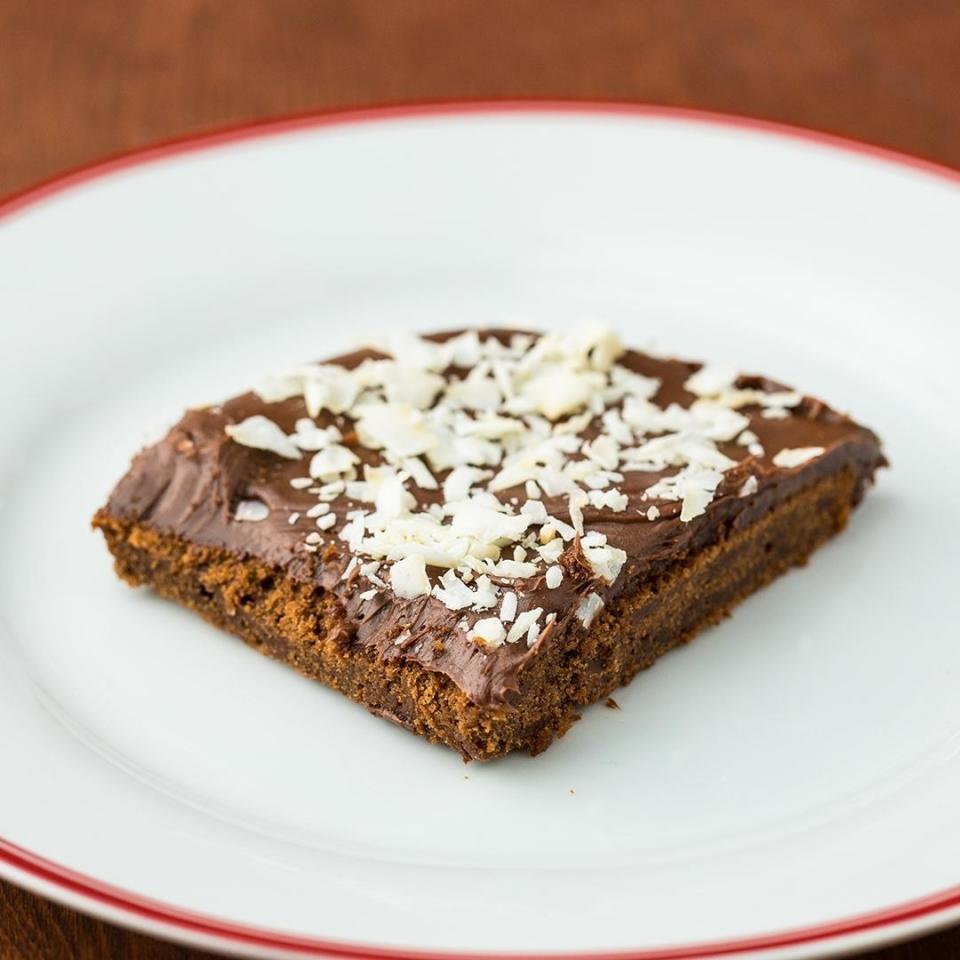 A square of sheet cake coated in thick chocolate sauce and topped with coconut