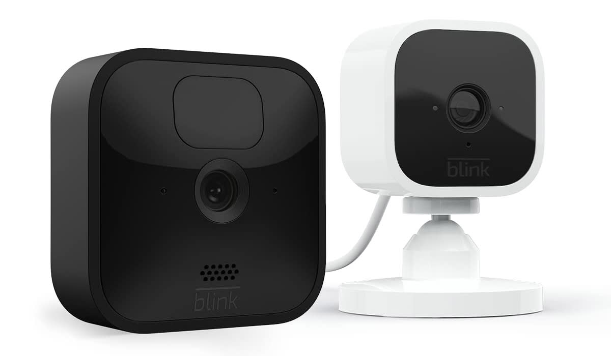 A square wireless camera next to a smaller, white wired camera on a pedestal. 