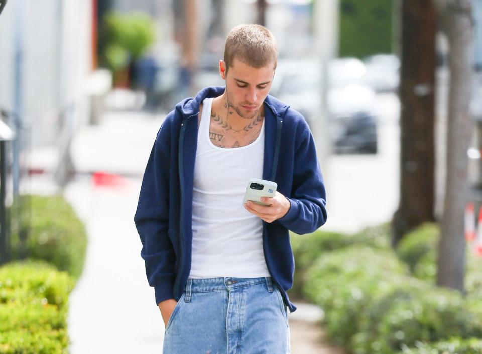 justin bieber walking down a street looking at his phone
