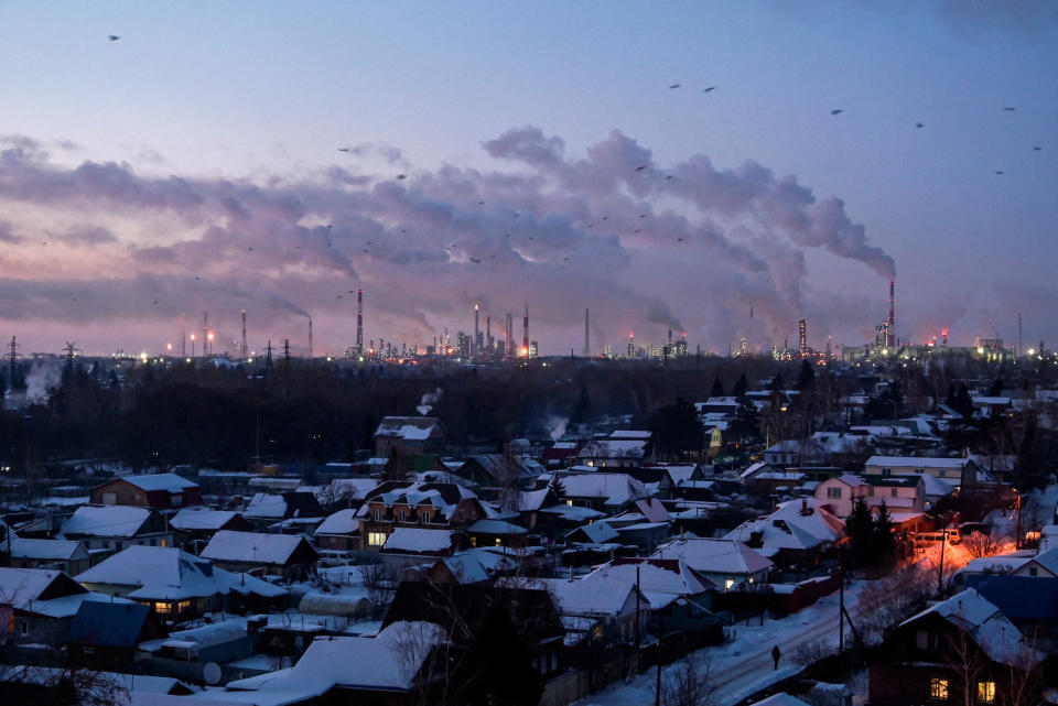 Pájaros vuelan por encima de los edificios mientras los gases de combustión y el vapor salen de las chimeneas de una refinería de petróleo durante la puesta de sol en un día helado en la ciudad siberiana de Omsk, Rusia, 8 de febrero de 2023. (REUTERS/Alexey Malgavko/Foto de archivo)