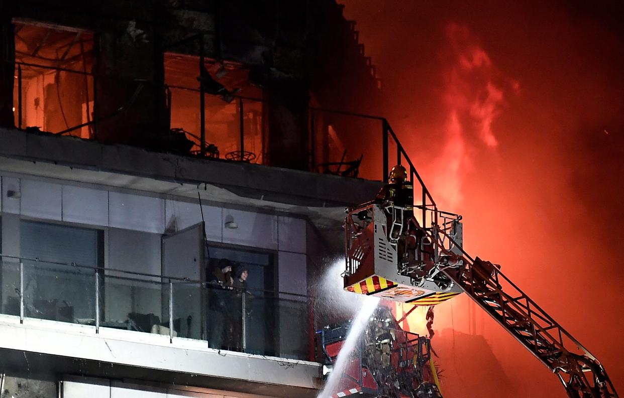 Two residents stand on a balcony, prior to being rescued, as firefighters battle a huge fire raging through a multistorey residential block in Valencia on February 22, 2024. Spanish firefighters were battling a huge fire raging through a multistorey residential block in the eastern port city of Valencia today, the emergency services said.