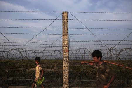 A Rohingya boy and a man walk along the fence separating Myanmar and Bangladesh as they return from a fish market in Maungdaw town in northern Rakhine State November 11, 2014. REUTERS/Minzayar