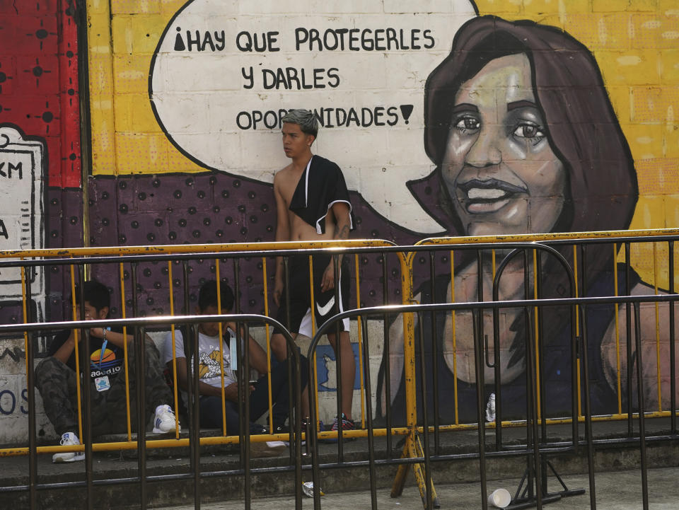 Migrants wait to apply for legal migration permits next to a mural that reads in Spanish "We must protect them and give them opportunities!" outside the National Immigration Institute in Tapachula, Chiapas state, Mexico, Tuesday, Oct. 4, 2022. At every step in a complicated process, opportunists are ready to provide documents or counsel to migrants who can afford to speed up the system, and who don’t want to risk their lives packed in a truck for a dangerous border crossing. (AP Photo/Marco Ugarte)