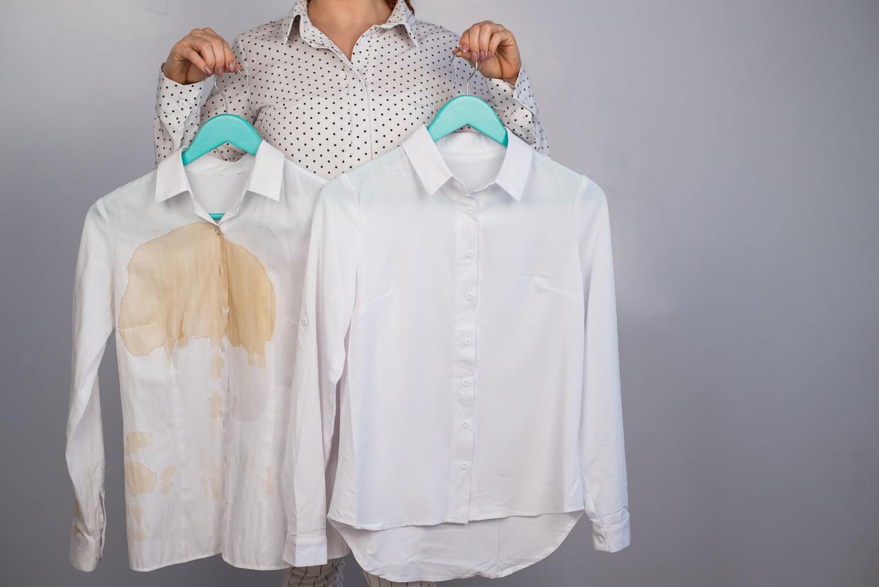 A woman compares two white shirts before and after washing. The girl is holding one blouse, clean and ironed, and the other, dirty with coffee stains.
