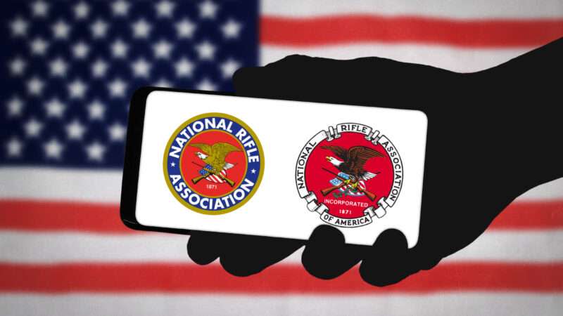 A hand holds a smartphone, displaying two different logos of the National Rifle Assocation (NRA), against a background of the American flag.