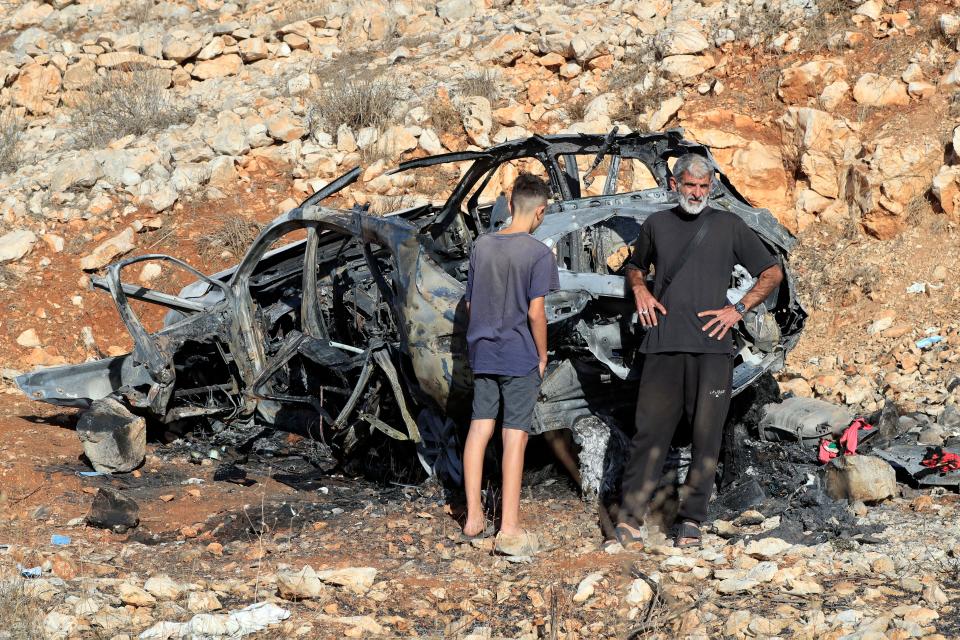 People stand next to the damaged car that hit by an Israeli airstrike in the town of Ainata, a Lebanese border village with Israel in south Lebanon, Monday, Nov. 6, 2023. An Israeli airstrike in south Lebanon on Sunday, Nov. 5, 2023 evening killed four civilians, including a woman and three children, raising the likelihood of a dangerous new escalation in the conflict on the Lebanon-Israel border. (AP Photo/Mohammed Zaatari)