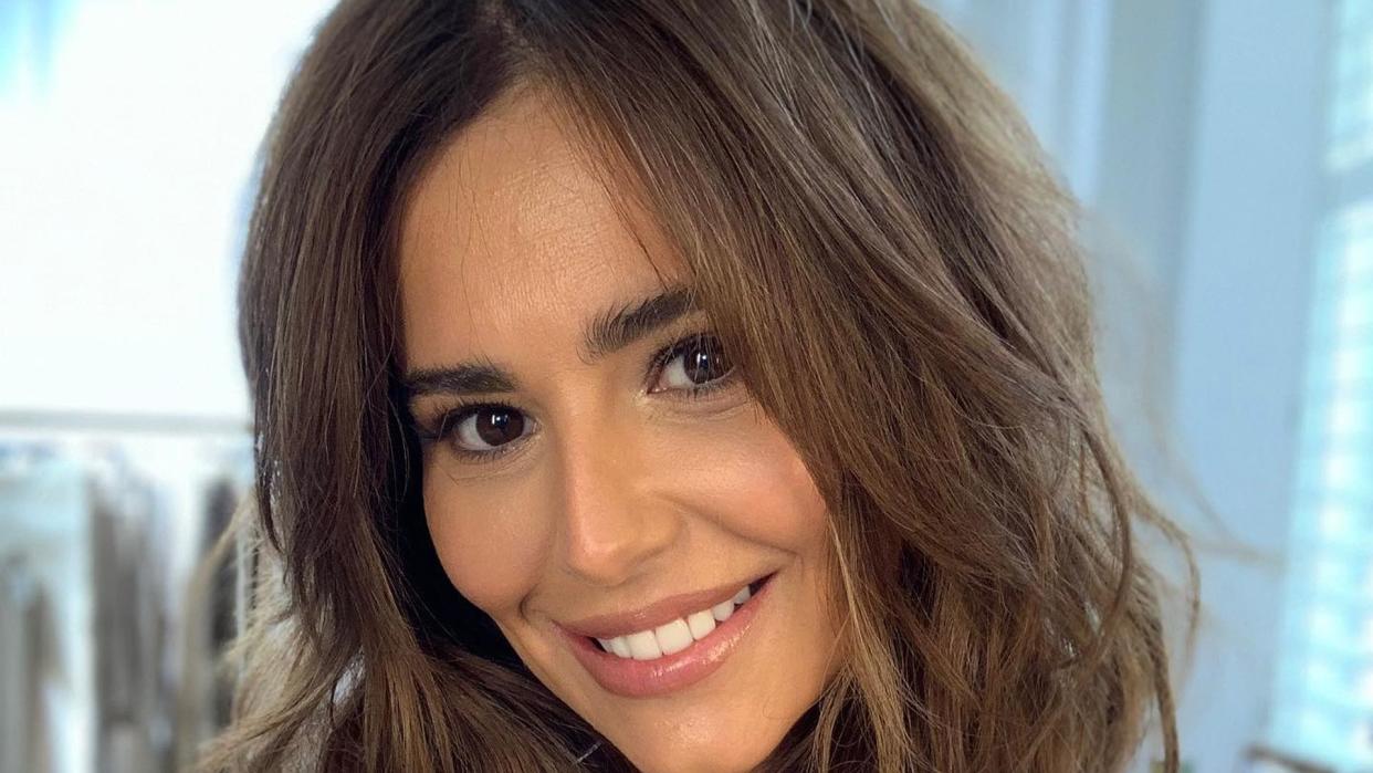 A close-up photo of Cheryl Cole smiling in an oversized shirt 