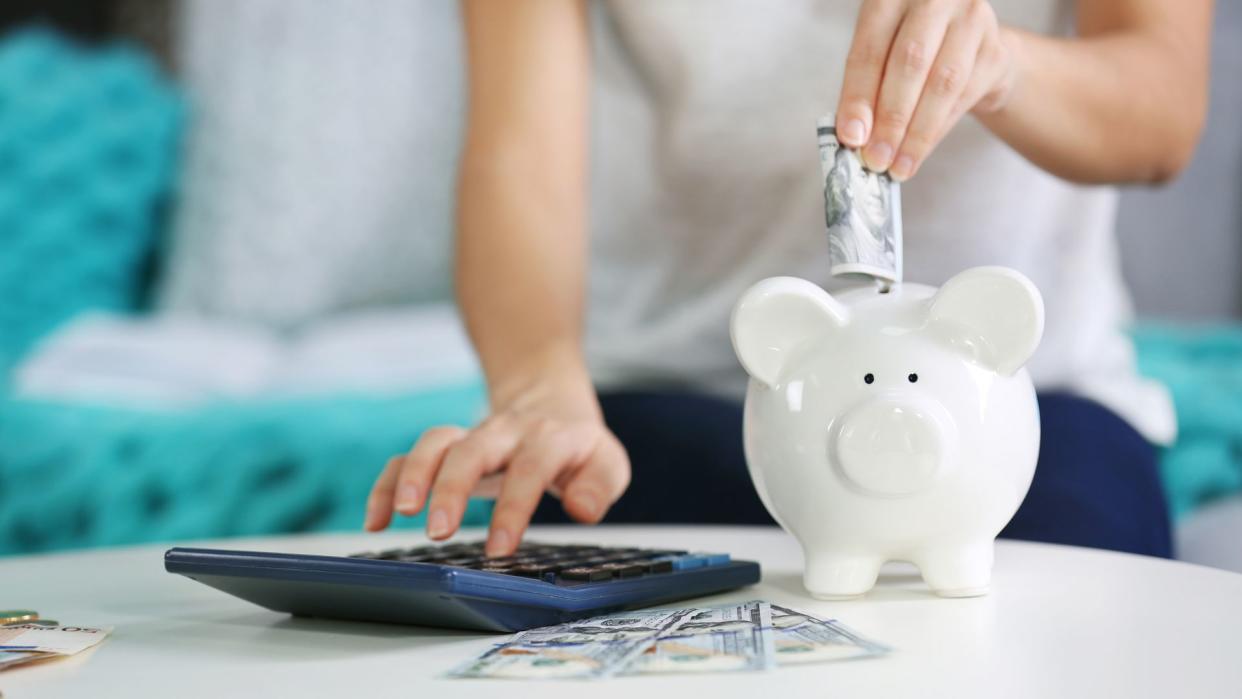 Hand putting money into piggy bank and counting on calculator closeup