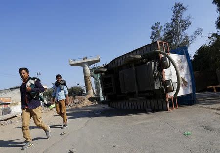 People walk past an overturned mobile urinal during a demonstration by members of the Jat community in Bahadurgarh in Haryana , February 21, 2016. REUTERS/Adnan Abidi