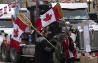 Surrounded by trucks, two protesters carry canoe paddles as flagpoles, Wednesday, Feb. 16, 2022 in Ottawa. Trucks in Canada that have been clogging crossings at the U.S. border for more than two weeks have abandoned all but one of their blockades. Canadian authorities say they're confident that protesters at the crossing in Manitoba will be gone by Wednesday.(Adrian Wyld/The Canadian Press via AP)