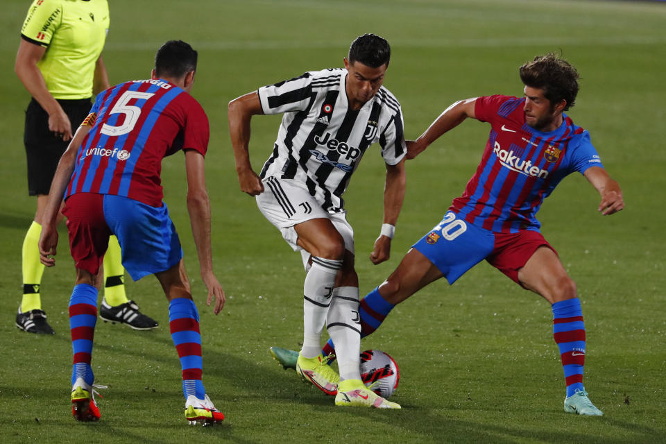 El delantero de la Juventus Cristiano Ronaldo (centro) maniobra entre Sergio Busquets (izquierda) y Sergi Roberto del Barcelona durante el partido por el trofeo Joan Gamper en Barcelona, el domingo 8 de agosto de 2021. (AP Foto/Joan Monfort)