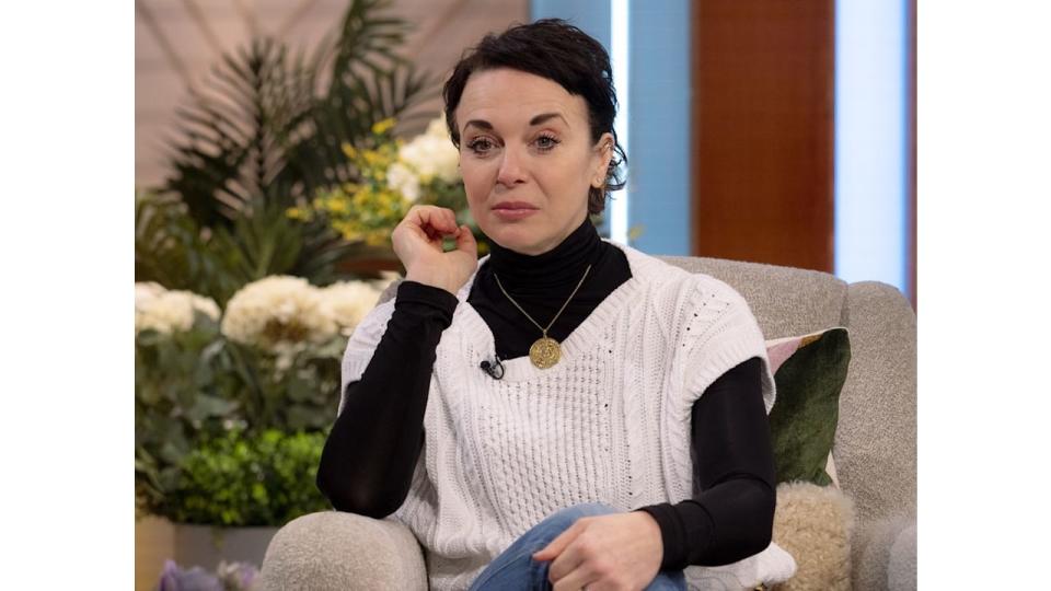 Amanda Abbington looking sad in a white cardigan and black turtleneck