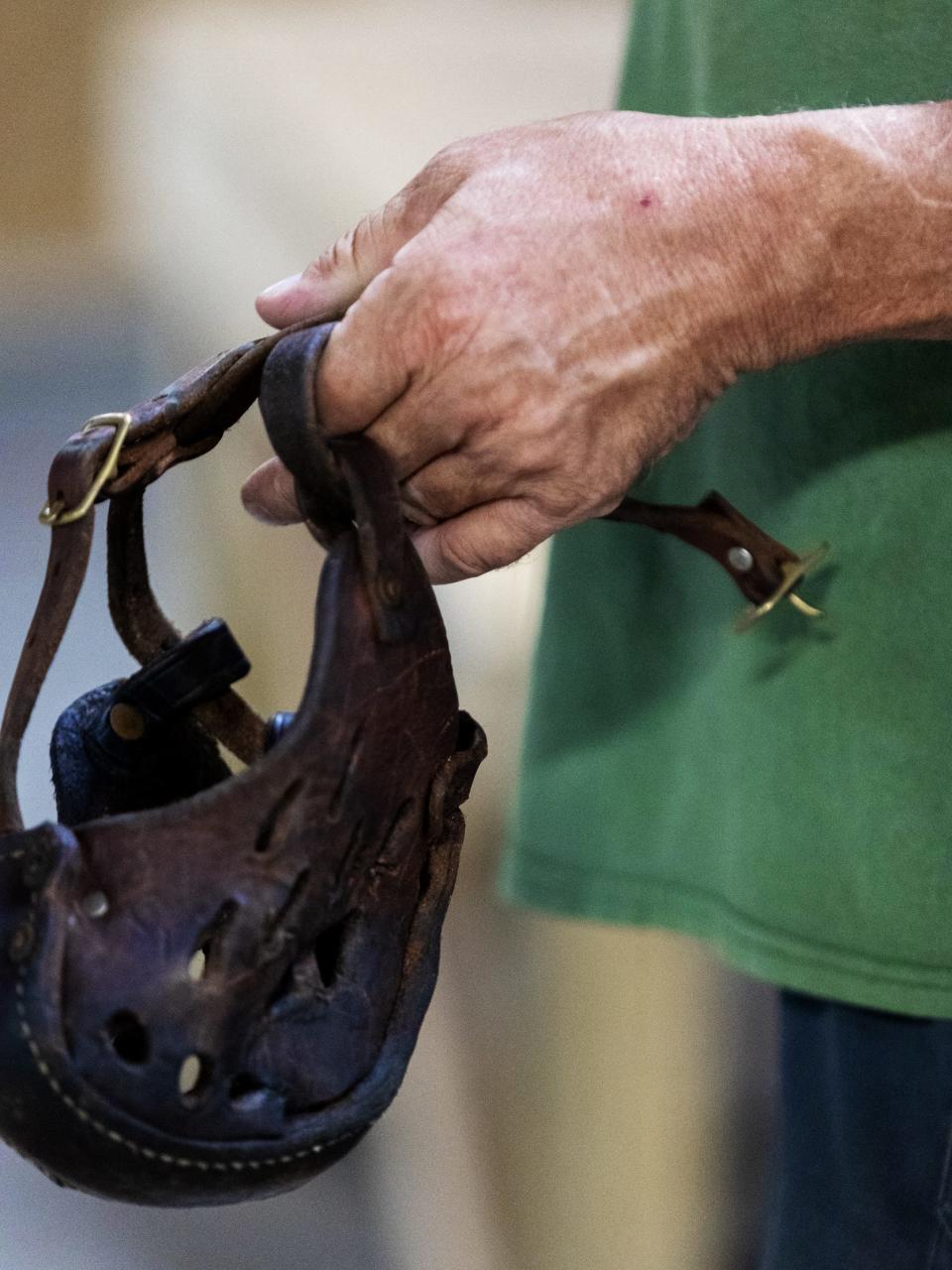 A man's hand holds a leather dog muzzle.