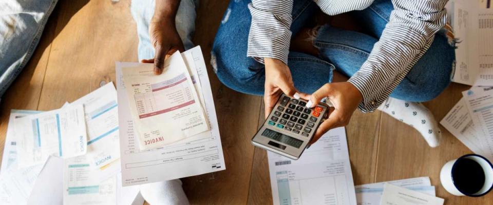 View of couple sitting on the floor from above with pile of bills and holding calculator