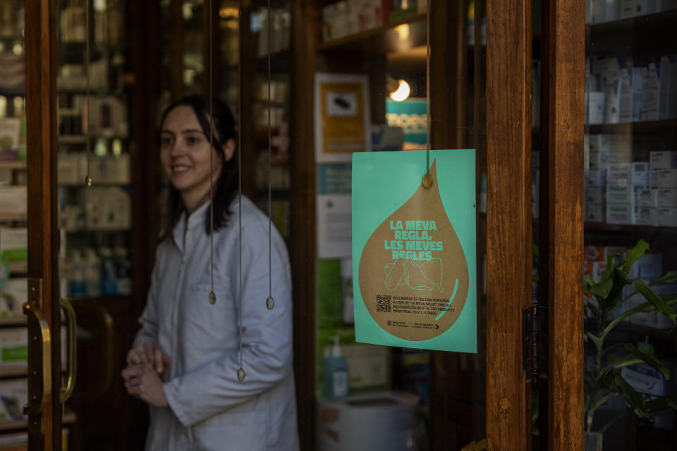 A pharmacist waits for customers next to windows where an advertisement for the new campaign of the Catalan government where you can read "my period, my rules" has been placed, inside a pharmacy in Barcelona, Spain, Tuesday, March 5, 2024. Spain's Catalonia region rolled out this week a pioneering women's health initiative that offers millions of women reusable menstruation products for free. Some 2.5 million women in northeast Spain can receive one menstrual cup, one pair of underwear for periods, and two packages of cloth pads at local pharmacies free of charge. (AP Photo/Emilio Morenatti)