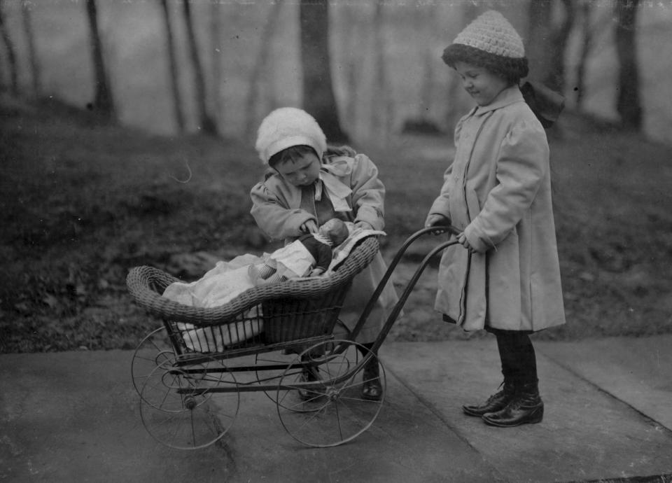 Two young girls play a Campbell Soup Kid doll, New York, New York, March 1912. One pushes it in a pram while the other looks at it with come concern. (Photo by Lewis W. Hine/Buyenlarge/Getty Images)