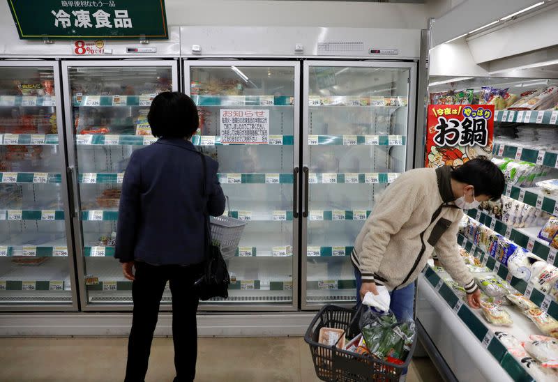 Un comprador con una mascailla junto a un estante vacío de alimentos congelados en un supermercado de Tokio, Japón