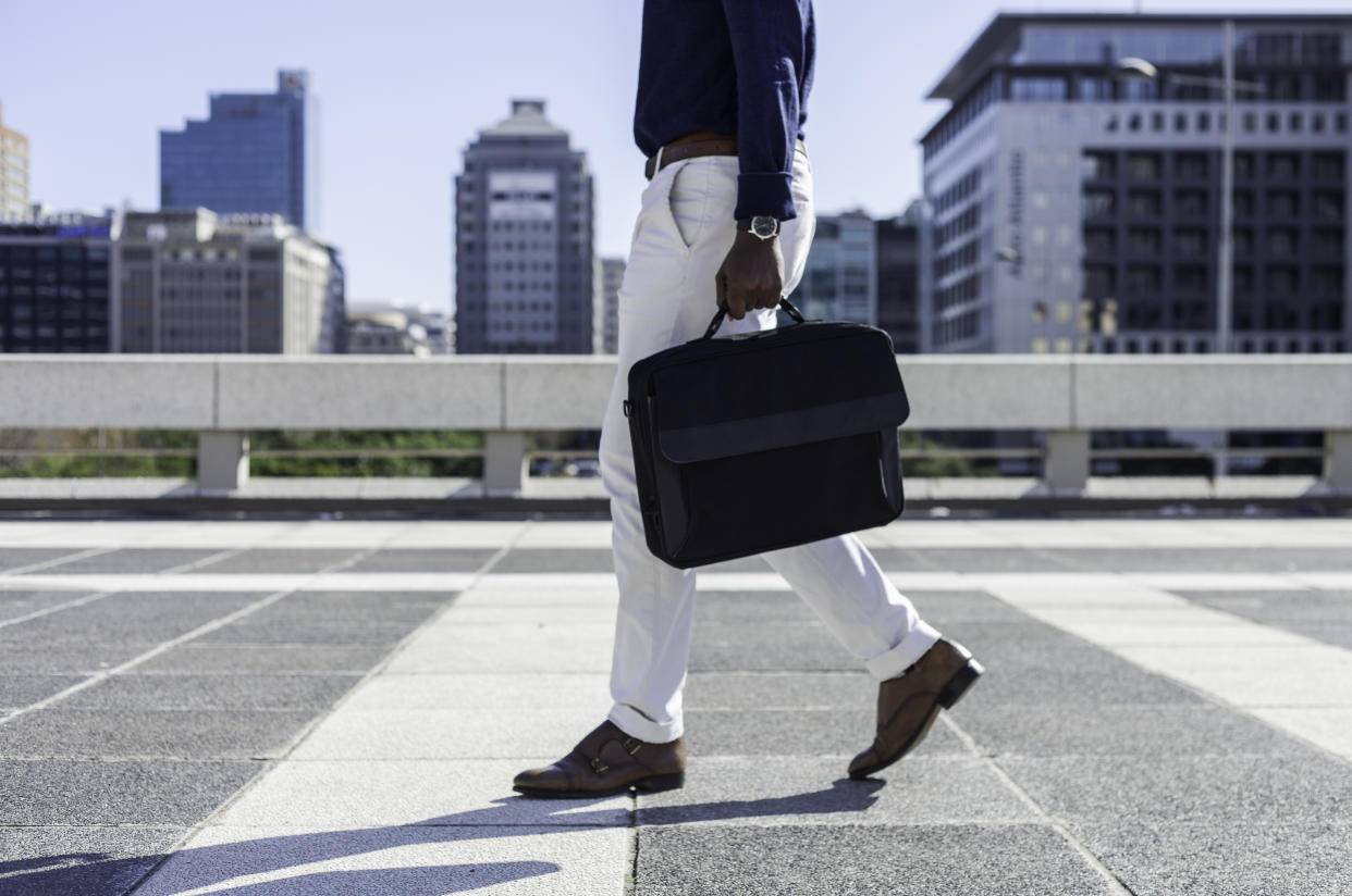 Mid adult African businessman walking through the city holding his laptop bag, the man is well dressed and the image is taken from the waist down.