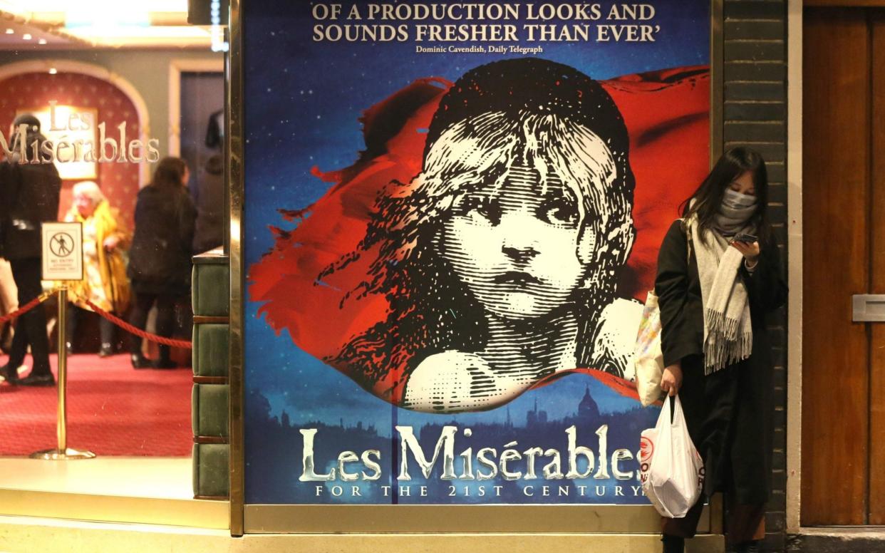 A woman wearing a face mask waits for an evening show of "Les Miserables" at Queen's Theatre on March 12, 2020 - Getty Images