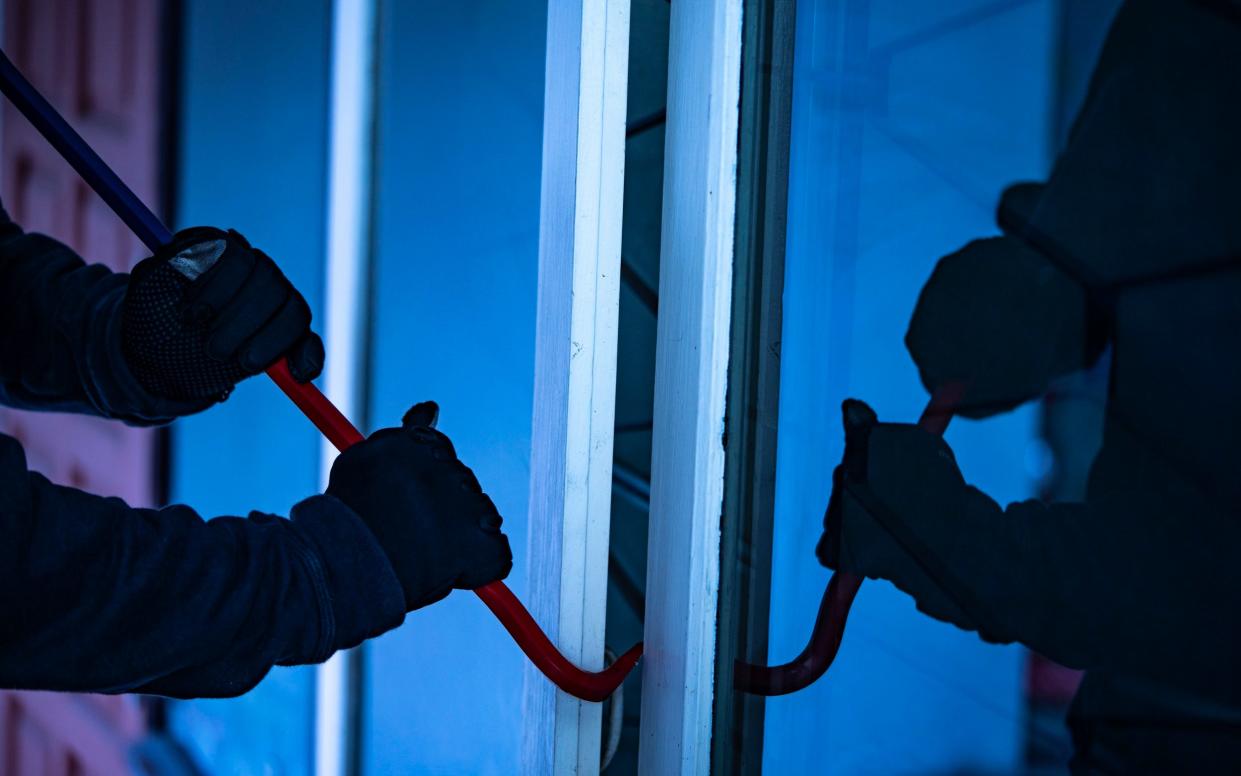 Burglar with crowbar trying break the door to enter the house