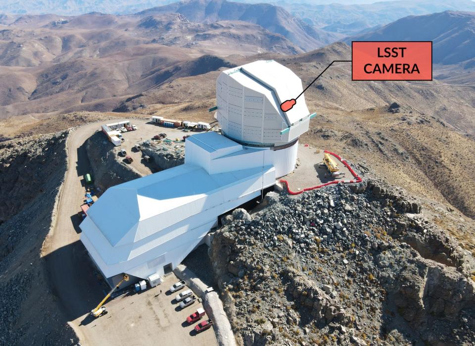 rubin observatory, a white box-shaped building with a telescope dome on the driveway, located on the top of a mountain surrounded by brown mountains