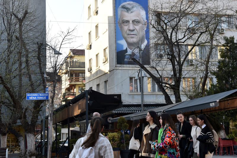 People walk near a banner displaying former Kosovo President Hashim Thaci, in Pristina