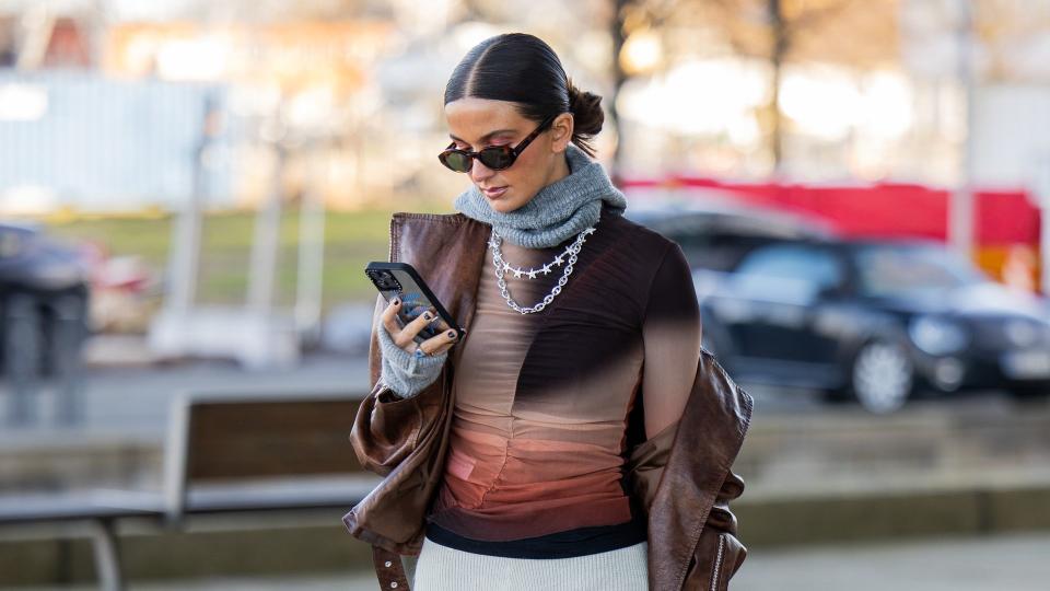 A guest wears white micro shorts, tights, brown top, animal print bag, black boots and a grey scarf 