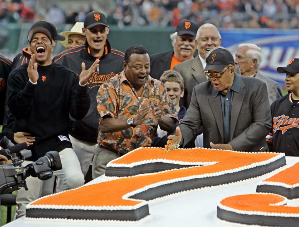 FILE - Willie Mays, right, uses his hand to chop through a large birthday cake presented in honor of his 75th birthday before the start of the San Francisco Giants baseball game against the Los Angeles Dodgers in San Francisco, in this Friday, May 12, 2006, file photo. Giants' Jose Vizcaino, left, laughs and former Giant and current broadcaster Tito Fuentes, center, applauds. Mays turns 90 on Thursday, May 6, 2021.(AP Photo/Eric Risberg, File)