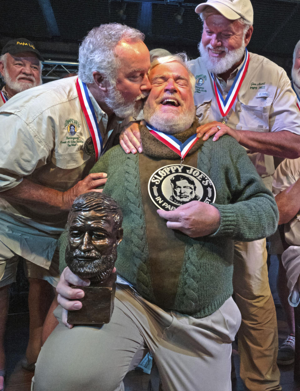 In this Saturday, July 22, 2023, photo provided by the Florida Keys News Bureau, Zach Taylor, left, and Jon Auvil, right, congratulate Gerrit Marshall, center, for winning the annual Hemingway Look-Alike Contest at Sloppy Joe's Bar in Key West, Fla. After 11 years of competing Marshall, a Madison, Wisc., resident, finally achieved success on his 68th birthday. The competition was a highlight of the annual Hemingway Days festival that ends Sunday, July 23. Ernest Hemingway lived in Key West throughout most of the 1930s. Taylor won in 2021, while Auvil was the 2022 winner. (Andy Newman/Florida Keys News Bureau via AP)