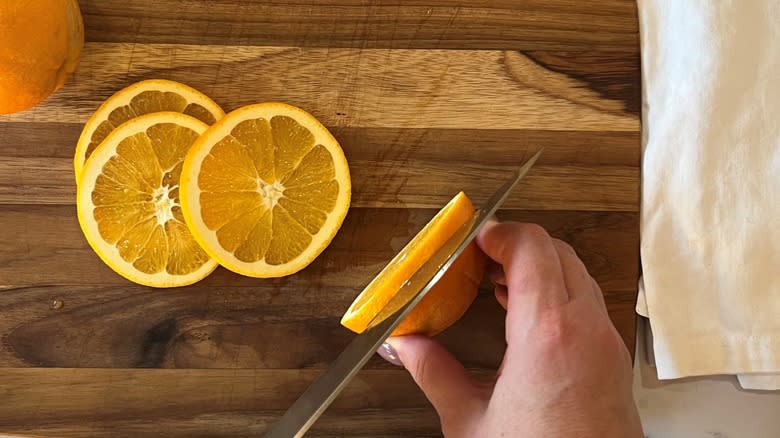 hand slicing oranges on wooden board