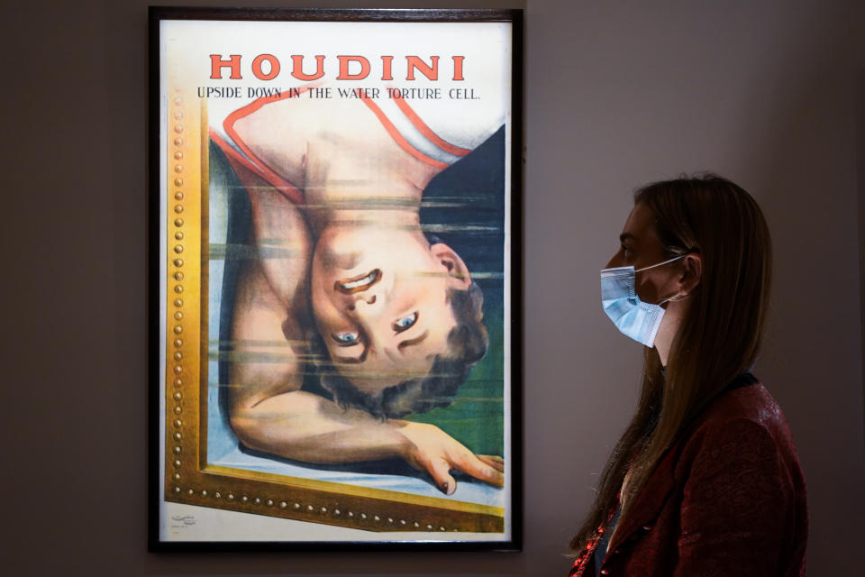 <p>A member of Sotheby's auction house staff stands next to Harry Houdini Upside Down in The Water Torture Cell poster, part of a collection of items belonging to celebrity magician Ricky Jay which is set to go under the hammer at Sotheby's in New York on October 27 and 28. Picture date: Friday September 24, 2021. The collection includes early and rare books on magic, a trove of Harry Houdini posters and 18th century playbills.</p>
