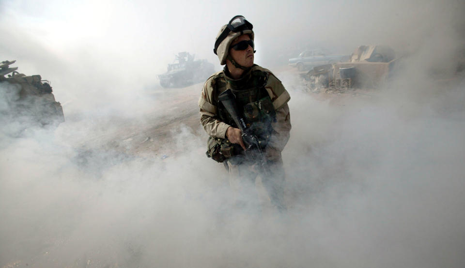 U.S. Army Spc. Jeffrey Ward, a medic with the 1st Cavalry Division, 1st Brigade, 1-12 Cav. from Fort Hood, Texas, stands guard in a haze of smoke during a cordon and search in a neighborhood outside of Sadr City on Aug. 15, 2004 in Baghdad, Iraq.