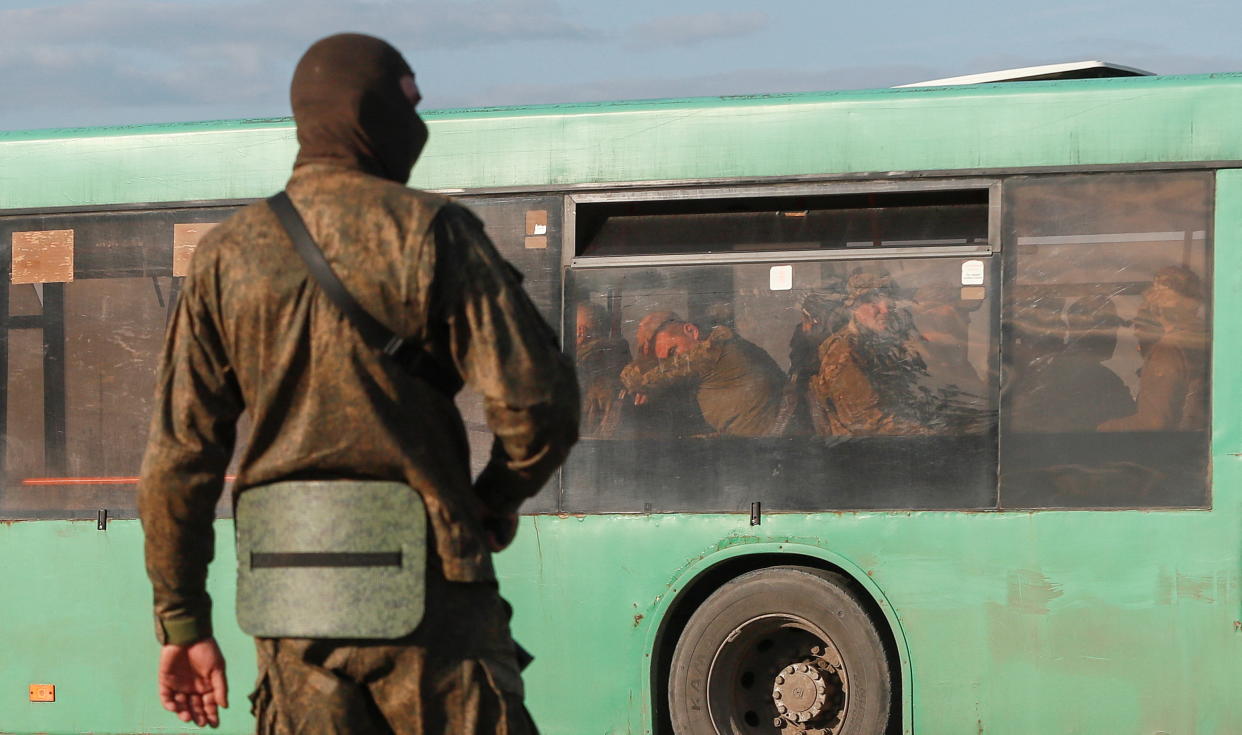 A pro-Russian service member stands guard near a bus carrying Ukrainian soldiers.