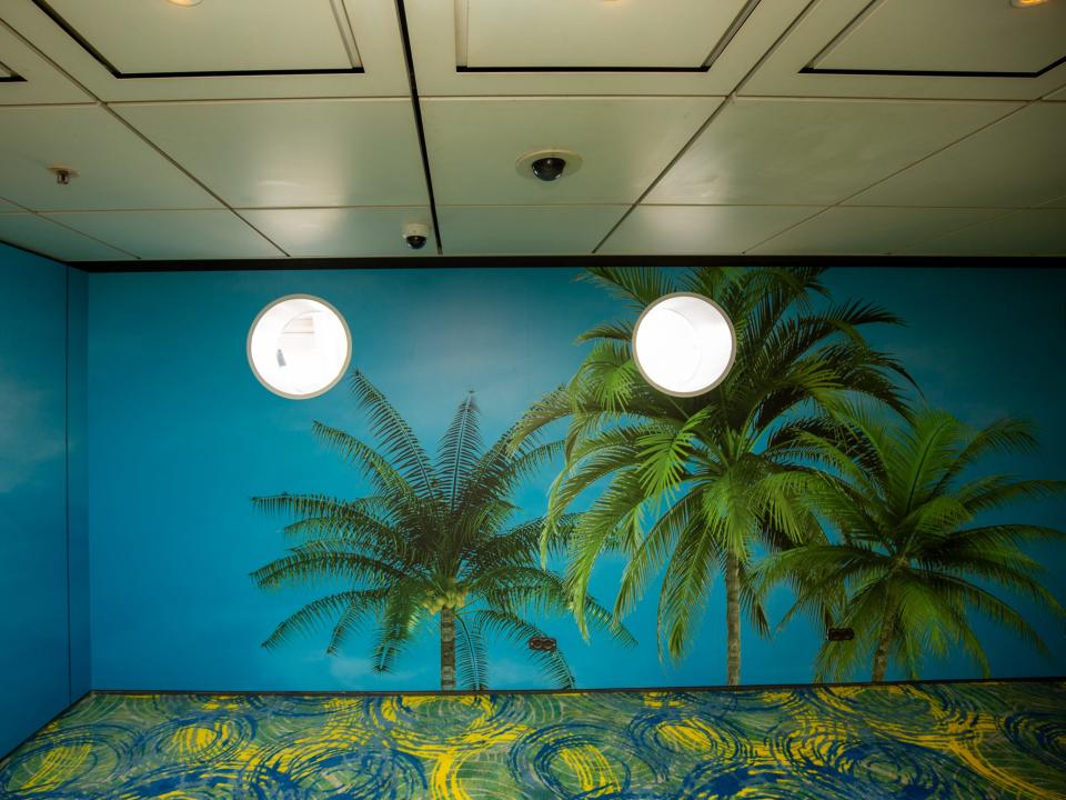 A wall with a graphic of palm trees and two windows.