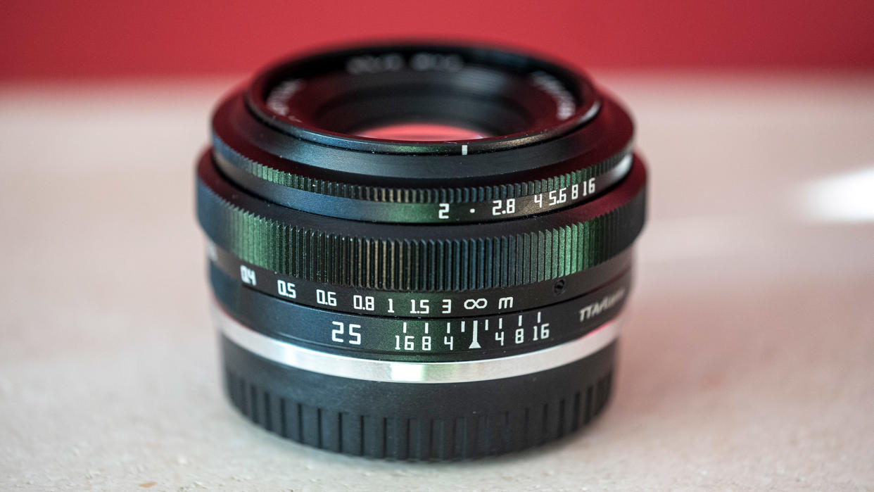  The TTArtisan 25mm f/2 lens on a stone shelf with red wall behind it. 