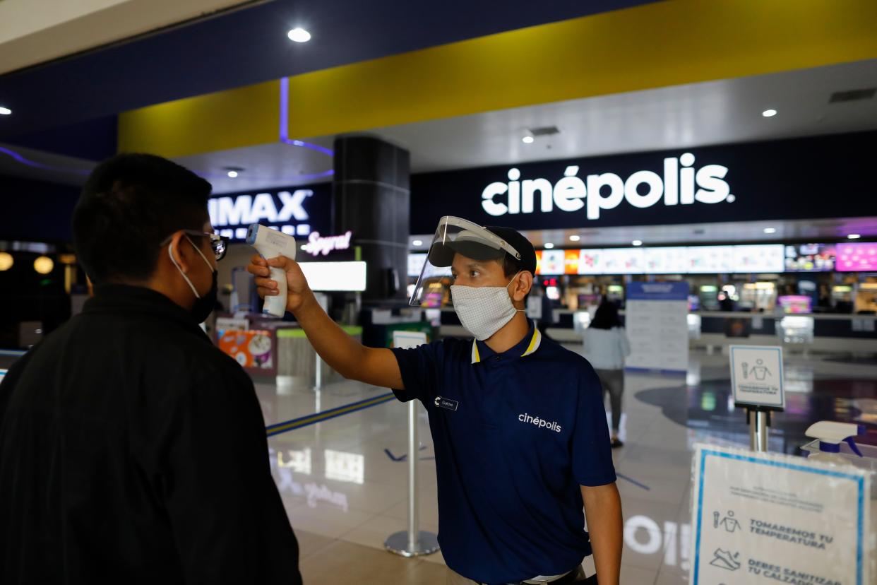 Cinema worker Gustavo Angel Oropeza Alvarez, 21, takes the temperature of a man arriving at the Cinepolis movie theater in Forum Buenavista mall in Mexico City, Mexico on Wednesday, Aug. 12, 2020. After being closed for nearly five months amidst the ongoing coronavirus pandemic, movie theaters in the capital reopened Wednesday at 30% capacity.