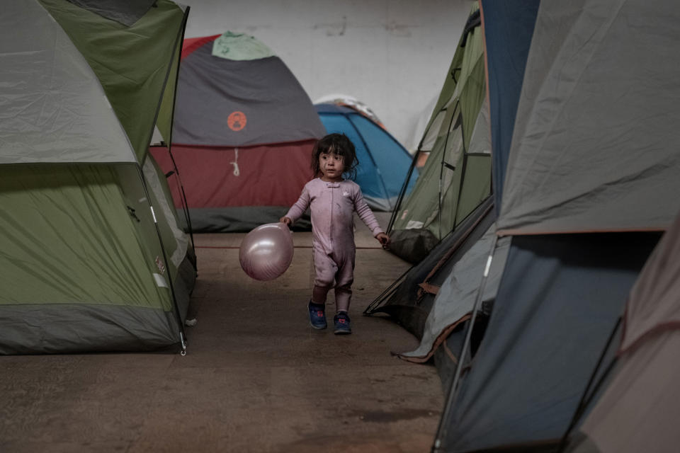 FILE - In this Jan. 2, 2019, file photo, a girl holds a balloon as she walks among tents inside an empty warehouse used as a shelter set up for migrants in downtown Tijuana, Mexico. The Trump administration expects to launch a policy as early as Friday, Jan. 25, 2019, that forces people seeking asylum to wait in Mexico while their cases wind through U.S. courts, an official said, marking one of the most significant changes to the immigration system of Donald Trump's presidency. (AP Photo/Daniel Ochoa de Olza, File)