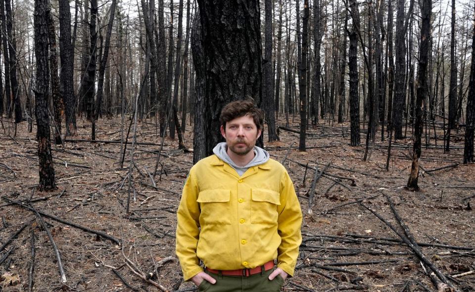 Pat MacMeekin, DEM's forest fire program manager, leans against a pitch pine tree at the Queen's River Preserve in Exeter that still shows the scars from last year's brushfire.