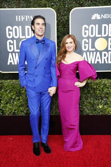 Sachan Baron Cohen in a bright blue suit holding hands and posing with Isla Fisher in a magenta gown with puff sleeves