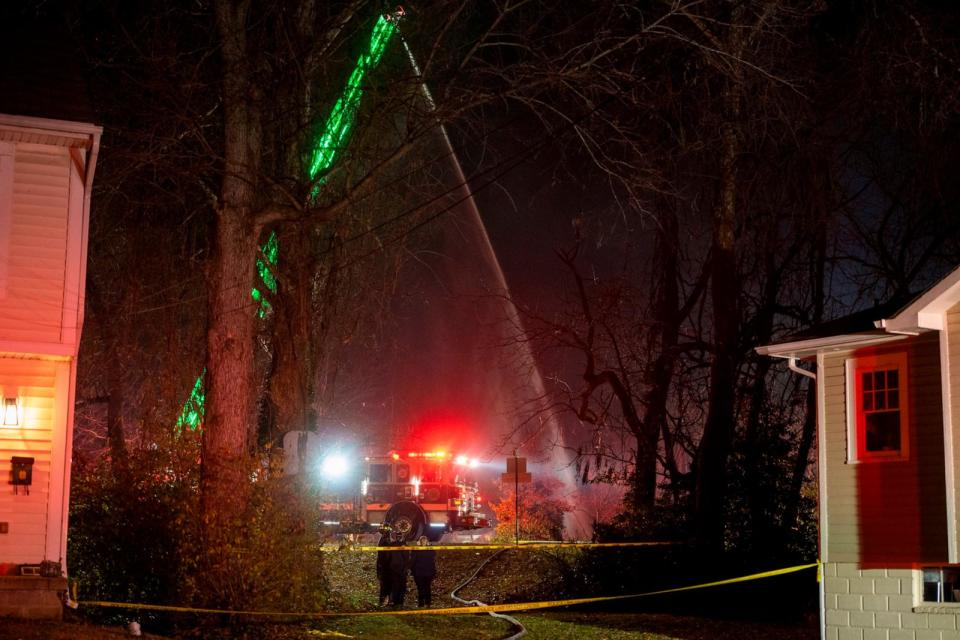 PHOTO: Fire and police officials walk around the scene of a house explosion as an Arlington County Fire Department ladder truck sprays water down on the remains of the building on Monday, Dec. 4, 2023, in Arlington, Va.  (Kevin Wolf/AP)