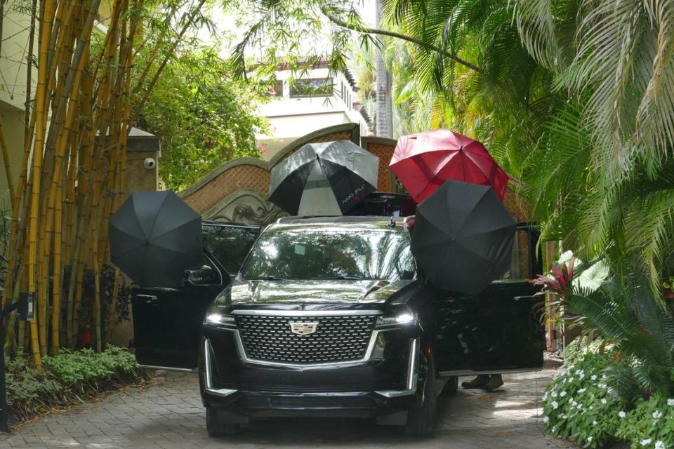 A man places umbrellas on a Cadillac Escalade outside Diddy’s 2 Star Island Drive mansion in Miami Beach on Wednesday, March 27, 2024. The home was raided by federal agents on Monday, March 25, 2024.