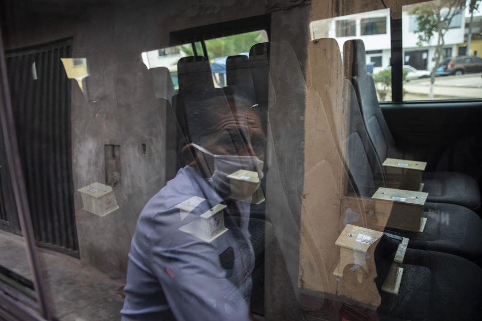 Piedrangel funeral home worker Anibal Rosado is reflected in a window of a company van as he prepares to help deliver to relatives, urns that contain the cremated ashes of people who are suspected to have died from the new coronavirus, in Lima, Peru, Monday, May 4, 2020. Edgard Gonzales, who owns the funeral home with his three brothers, says Piedrangel cremates all COVID-19 victims. (AP Photo/Rodrigo Abd)