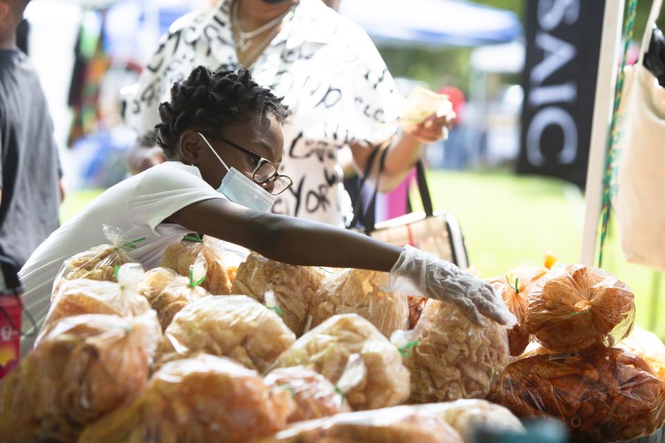 DeShawn Hill, 8, sets out pork skins at The Pork Skins Crew booth during Goombay on Sept. 4, 2021, in downtown Asheville.  Goombay, which celebrates its 40th anniversary this year, highlights African and Caribbean heritage in WNC.