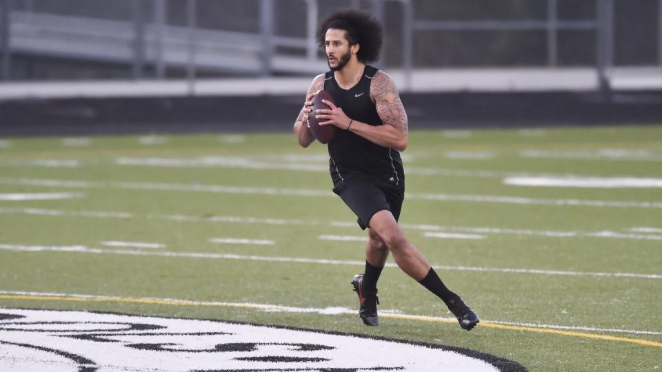 colin kaepernick wearing a black shirt and shorts, running and preparing to throw a football on a football field