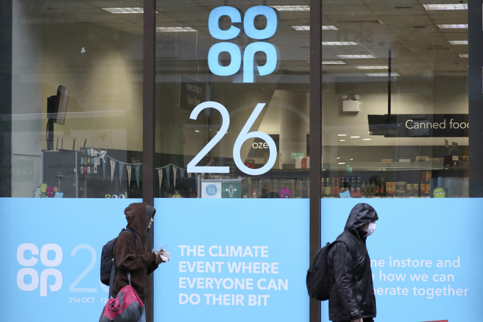 FILE - In this Oct. 29, 2021, file photo, pedestrians walk past a shop window advertising the COP26 climate conference in Glasgow, Scotland. Despite the concerns about the coronavirus from some of the delegates from around the world, the British government decided to hold an in-person conference, arguing that world leaders must act now to prevent catastrophic global warming — and that they will be more effective if they can talk face-to-face. (AP Photo/Scott Heppell, File)