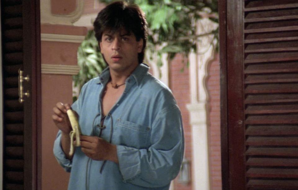 Actor Shah Rukh Khan pauses before a door while peeling a banana.