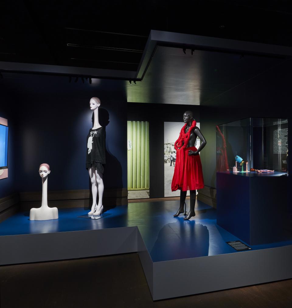 Within the 'Mirror Mirror' exhibit, an Ed Tsuwaki manikin with a swan-like long stands at the left beside a black manikin of Michelle Elie at the right.